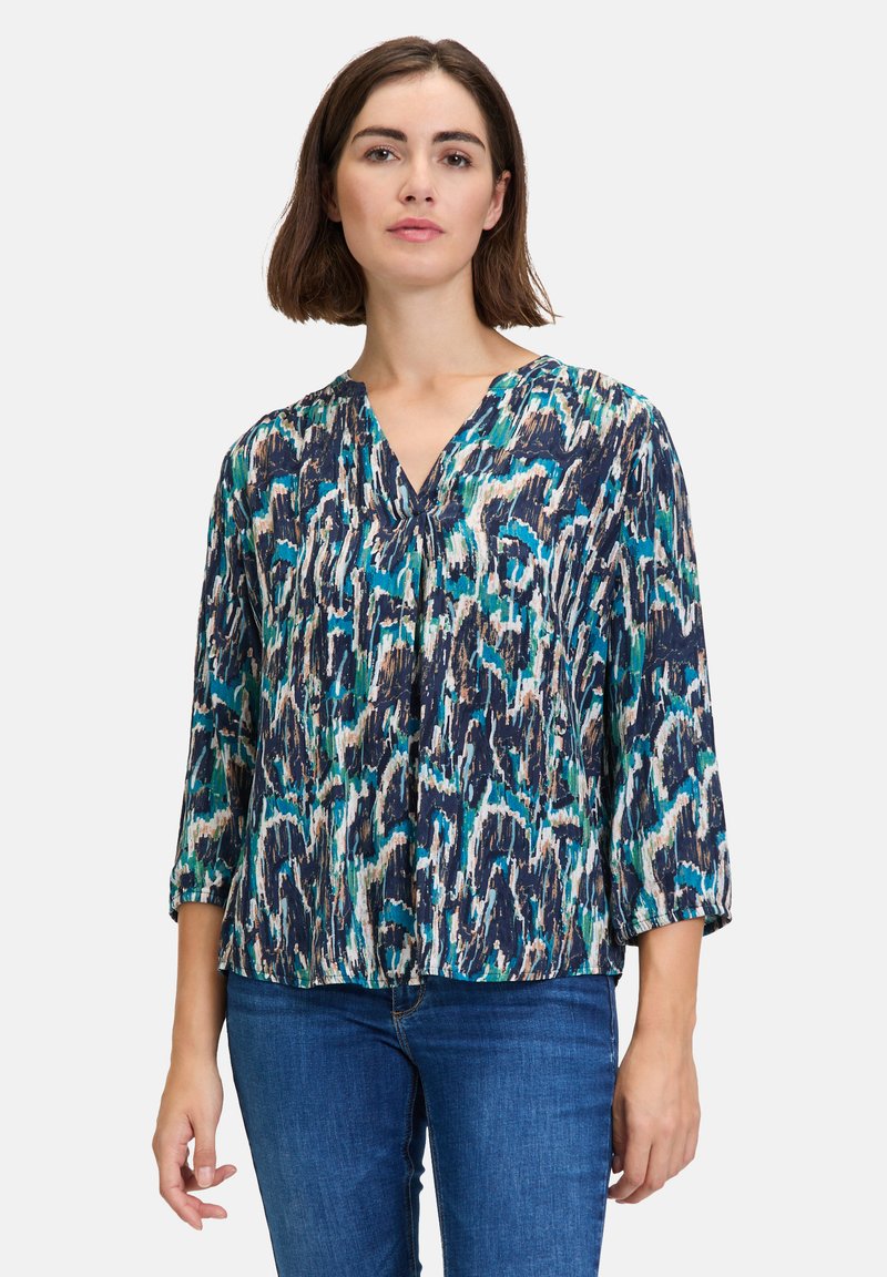 Blouse imprimée dans des nuances de bleu, vert et beige. Présente un décolleté en V et des manches trois-quarts. Tissu léger et texturé avec une coupe ample.