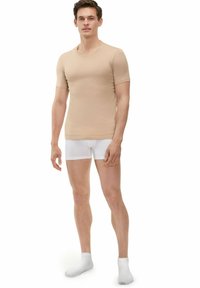 Beige strak aansluitend T-shirt met korte mouwen, gemaakt van een glad materiaal, gecombineerd met witte boxershorts en witte sokken. Eenvoudig ontwerp, zonder patronen.