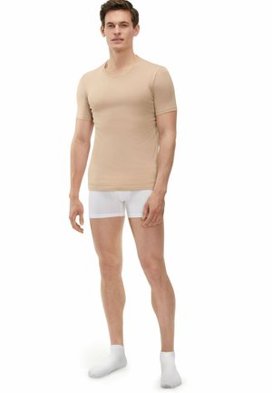 T-shirt beige ajustée à manches courtes en tissu lisse, associée à un short blanc et des chaussettes blanches. Design simple, sans motifs.