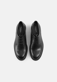 Black leather shoes with a smooth texture, featuring a minimalist design, lace-up closure, and a low-profile rubber sole.