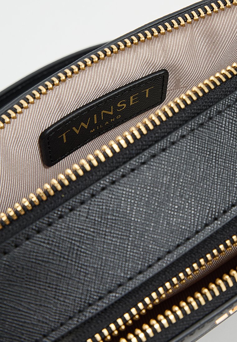 Wnętrze czarnej skórzanej torby z złotymi zamkami błyskawicznymi i materiałowym wykończeniem z delikatnym wzorem. Etykieta oznaczona "TWIIINSET MILANO."