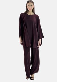 Burgunderrotes zweiteiliges Outfit mit locker sitzendem Oberteil und weitem Ärmel sowie passenden, weit geschnittenen Hosen aus weichem, glattem Stoff.