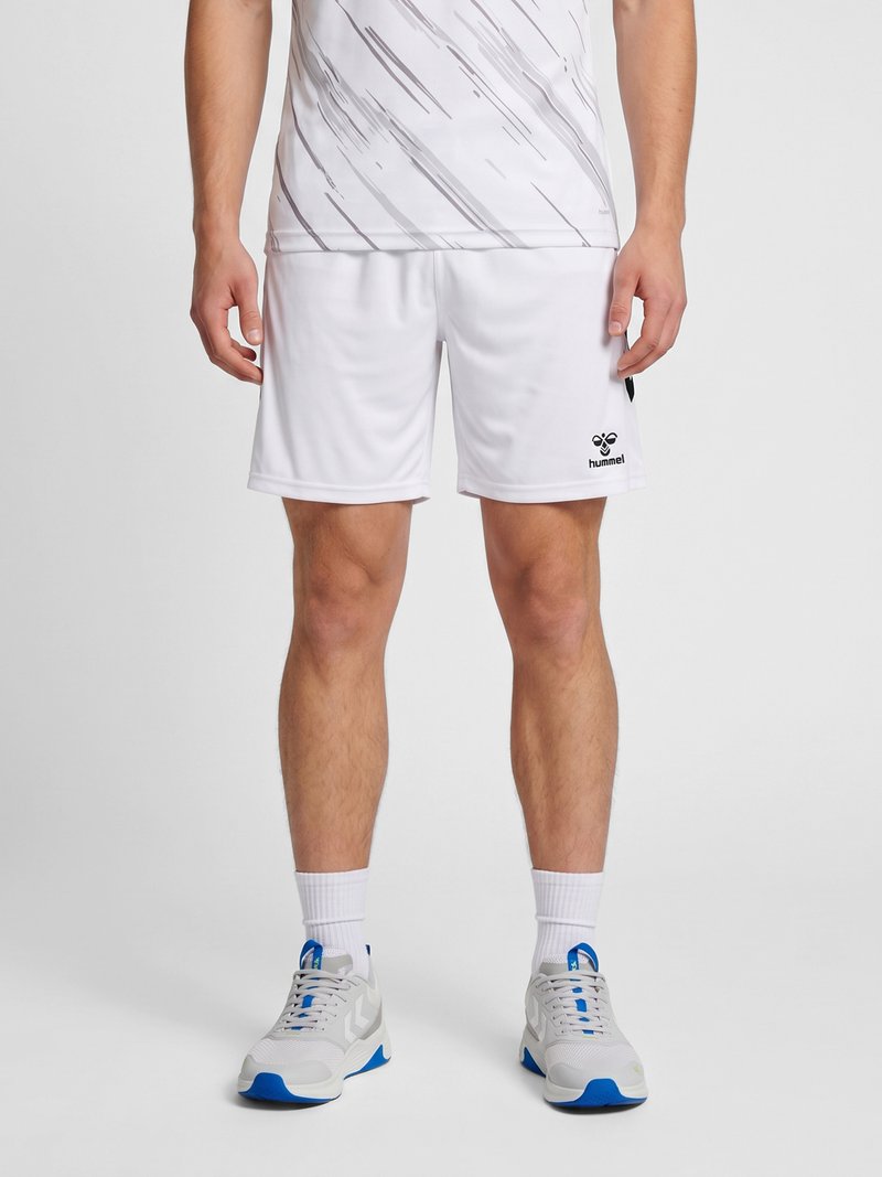 Mann trägt weiße Sportshorts mit schwarzem Logo am linken Bein, weiße hohe Socken und weiße und blaue Sportschuhe.