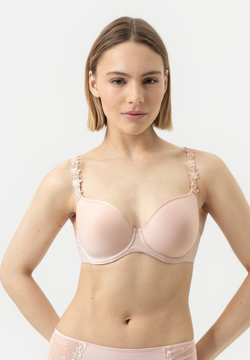 Vaaleanpunainen rintaliivi, jossa pehmeä kangas, tukevat kaarituet ja kukkavaatteen yksityiskohtia hihnoissa. Muotoilu sisältää muotoiltuja muotoja ja saumattomia kuppeja.