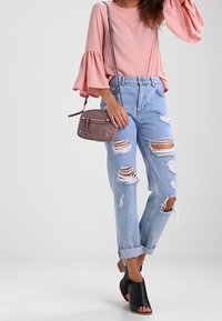 Vaaleanpunainen pitkähihainen pusero, jossa liehuvat kalvosimet, yhdistettynä revittyihin vaaleansinisiin farkkuihin. Asuun kuuluu mustat avokärkiset korkokengät ja pieni harmaa käsilaukku.