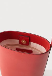 Czerwona skórzana torebka o gładkiej fakturze, z otwartym designem i złotym zapięciem na zatrzask. Wnętrze wyposażone w kieszeń na zamek oraz metkę marki.