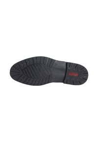 Semelle de chaussure en caoutchouc noir présentant un motif de grip texturé avec des crampons profonds et un logo central en relief de couleur rouge. Bords arrondis et conception durable.