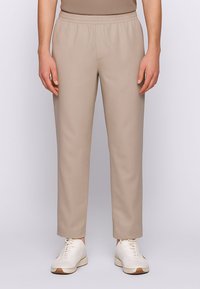 Pantaloni beige con vita elastica e gambe affusolate, realizzati in un tessuto liscio. Indossati con sneakers bianche con accenti marrone chiaro.