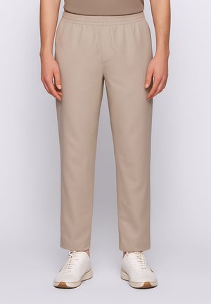 Pantaloni beige con vita elastica e gambe affusolate, realizzati in un tessuto liscio. Indossati con sneakers bianche con accenti marrone chiaro.