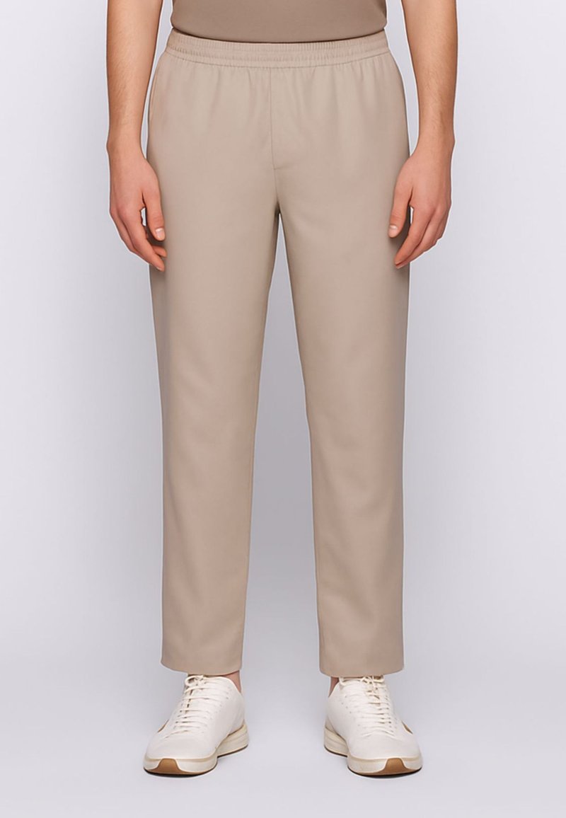 Pantaloni beige con vita elastica e gambe affusolate, realizzati in un tessuto liscio. Indossati con sneakers bianche con accenti marrone chiaro.
