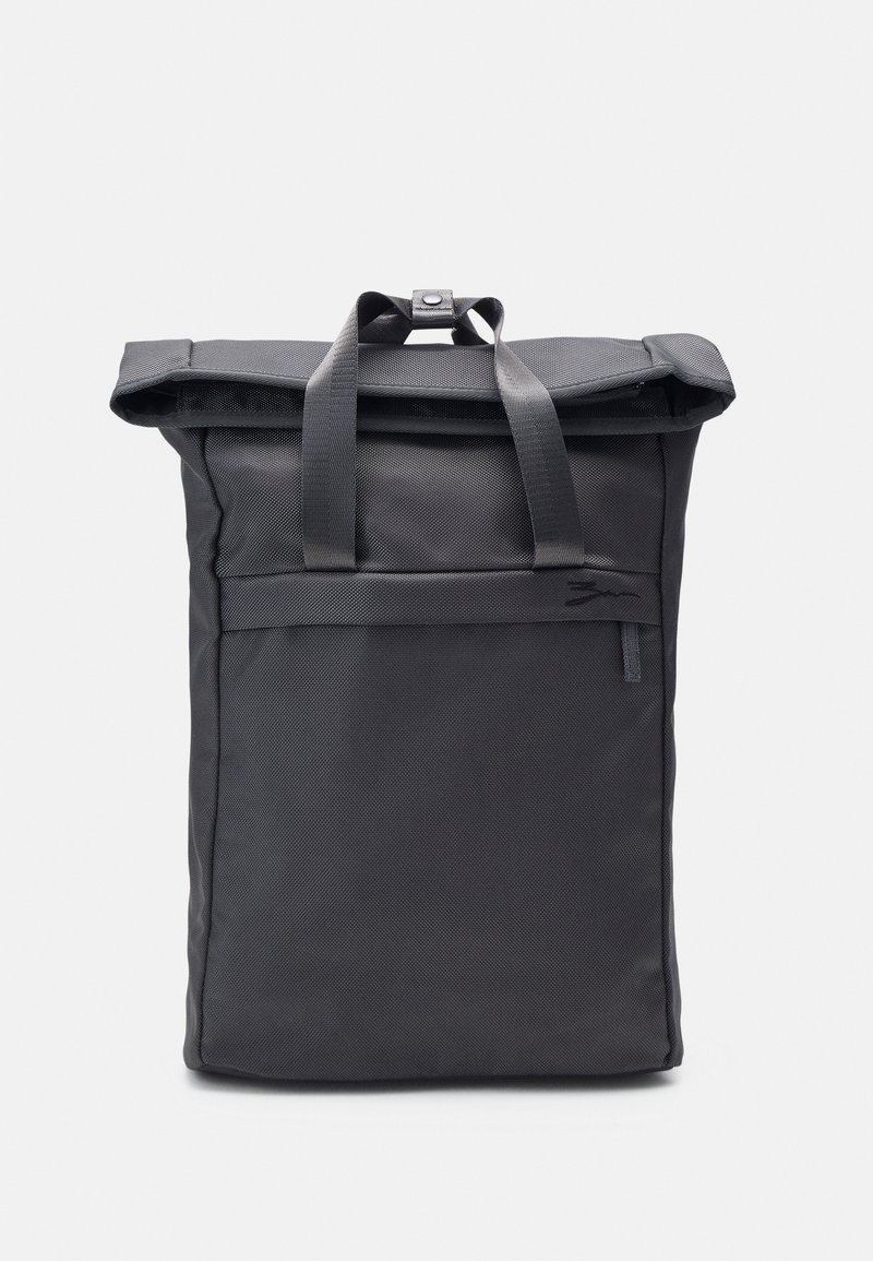 Sac à dos rectangulaire noir à rabat enroulable avec deux poignées et un fermoir à pression sur un fond uni.