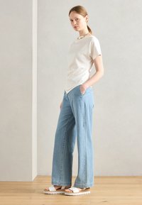 Light beige short-sleeve top, wide-leg light blue jeans, white platform sandals. Simple design with a relaxed fit and pocket details.
