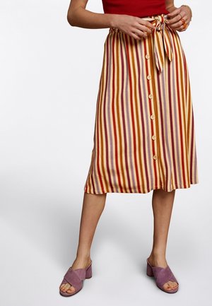 Woman wearing a vertical striped buttoned midi skirt with a waist tie and purple heeled sandals, standing against a plain white background.