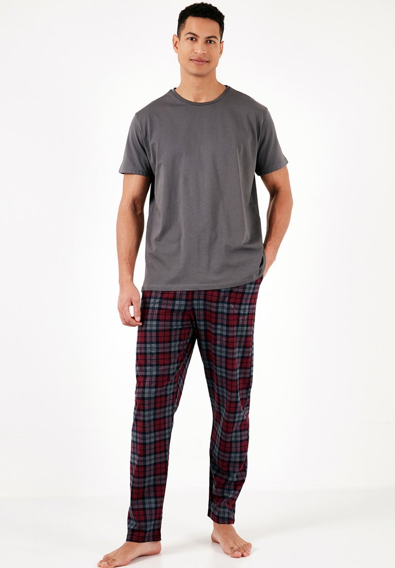 Grijze katoenen t-shirt gecombineerd met rode geruite pyjamabroek met blauwe en groene accenten. Model staat blote voeten tegen een effen achtergrond.
