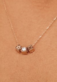 Collier doré avec trois pendentifs : une étoile, un cœur et un zircon cubique central. La chaîne est délicate avec un design de mailles fines.
