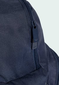 Marinblå ryggsäck med en texturerad tyg, med en svart dragkedjehandtag med en logotyp och en kurvig design för ergonomisk användning.