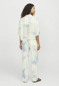 Lehká, zkrácená košile na knoflíky a odpovídající široké kalhoty v pastelově zelené s modrým tie-dye vzorem. Má krátké rukávy a boční kapsy.