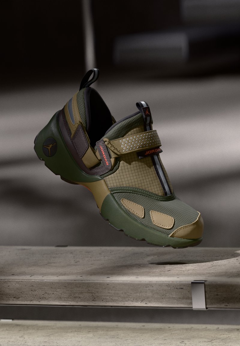 Grüne und beige Jordan-Sneaker mit Mesh- und Gittertexturen, Klettverschluss und Logodetail, über einer Betonoberfläche schwebend.