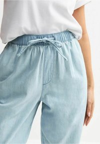 Vaaleansiniset farkuhousut, joissa on joustava vyötärö, säädettävä nyöri ja sivutaskut. Kangas vaikuttaa pehmeältä ja hengittävältä.