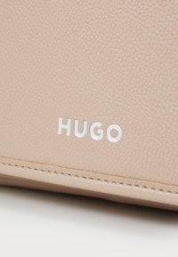 Portefeuille en cuir texturé beige avec logo "HUGO" en relief en blanc, présentant des bords lisses et des détails de couture subtils.