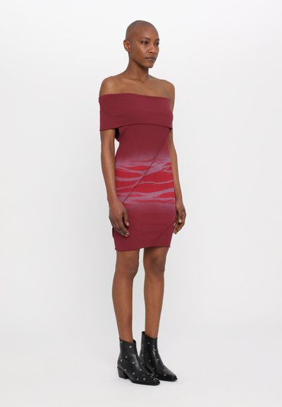 Abito aderente in borgogna con scollo off-the-shoulder e motivo rosso a gradiente. Presenta una texture a costine e un orlo dritto. Modello che indossa stivaletti neri alla caviglia.