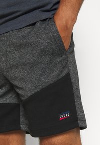 Grijze shorts met een gestructureerde afwerking, voorzien van een zwarte passe-partout aan de zijkant. Klein logo-label in blauw, rood en wit aan de zoom.
