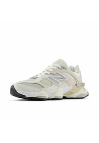 Jasnoszare i białe trampki New Balance z siateczkowymi panelami, zamszowymi nałożeniami, odblaskowym logo "N" oraz masywną podeszwą z czarnymi akcentami.