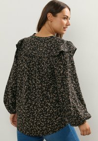 Blusa nera a maniche lunghe con motivo floreale in beige. Presenta spalle arricciate e una vestibilità morbida. Tessuto liscio con dettaglio arricciato sul retro.