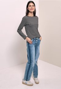 Striped black and white long-sleeve shirt paired with light blue wide-leg jeans and beige sneakers. Smooth fabric and casual cut.