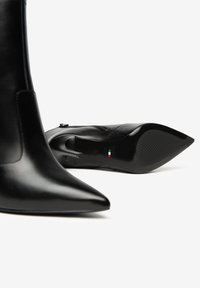 Zwarte leren enkellaarzen met een puntige neus, glanzende afwerking en een gewatteerde zool. Zijkant met ritsdetail en Italiaanse vlag insignia onderaan.