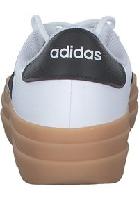 Białe sneakersy z czarnymi skórzanymi akcentami na pięcie oraz tkanym, siateczkowym językiem. Posiadają grubą, tanową gumową podeszwę. Logo „adidas” wyświetlane na biało.