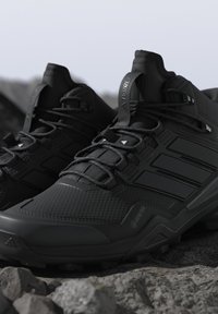 Zwarte Gore-Tex wandelschoenen met een gestructureerd oppervlak, stevige veters en robuuste zolen die op rotsachtig terrein liggen.