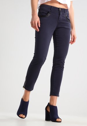 Mørkeblå smalle jeans med lynlåsåbninger ved anklerne og kontrasterende lommer foran, lavet af et strækbart materiale for ekstra komfort.