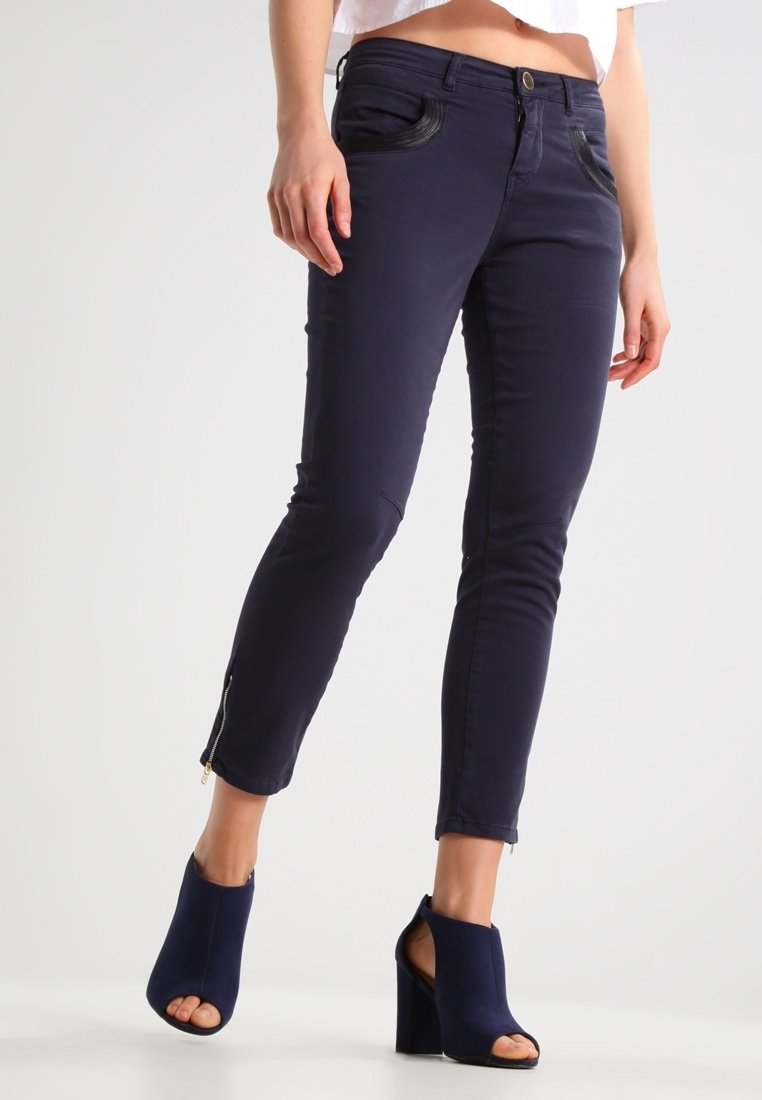 Vaqueros skinny azul marino con detalles de cremallera en los tobillos y acentos contrastantes en los bolsillos delanteros, confeccionados con un material elástico para mayor comodidad.