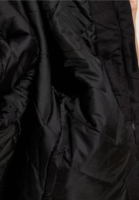 Černá péřová bunda uvnitř s prošívanou texturou. Disponuje hladkým, lesklým materiálem a viditelnými švy. Obsahuje zip a akcenty na suchý zip.