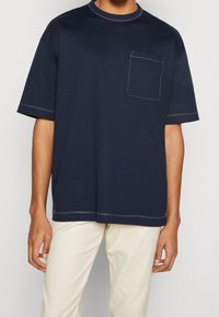 Granatowy bawełniany T-shirt z zaokrąglonym dekoltem, krótkimi rękawami, kieszonką na piersi i kontrastującymi detalami szwów.