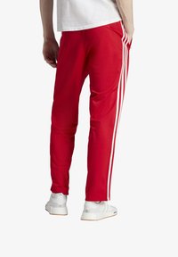 Rote Sporthosen mit weißen Seitenstreifen, tailliertem Schnitt, glatter Textur und Taschen; getragen mit weißen Sportschuhen.