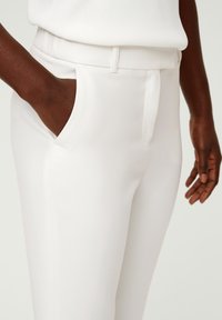 White tailored pants with a smooth texture, featuring a front crease, side pockets, and a fitted waistband for a streamlined look.