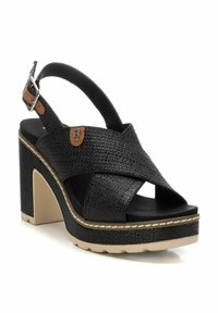 Sandalias de plataforma negras con un diseño de tiras cruzadas texturadas, correa ajustable en el tobillo y suela beige con un detalle de costura en contraste.