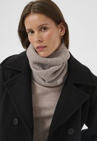 Heledast hall varruline soonikuga kraega sall, mis on kantud beeži kampsuni peale, mida täiendab must mantel suurte nööpide ja tipuservadega kraega.