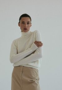 Kremowy sweter z golfem, wykonany z miękkiej dzianiny, z długimi rękawami i ściągaczami, w połączeniu z beżową spódnicą.