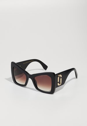 Black oversized sunglasses with gradient brown lenses, featuring a square frame and golden hardware accent on the outer side.