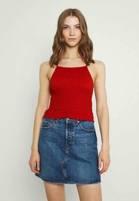 Top halter em malha vermelha, combinado com uma saia mini de denim azul clara. O conjunto apresenta um design ajustado e o clássico estilo de cinco bolsos.