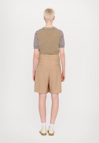 Beige tailored shorts with two back pockets, paired with a striped short-sleeve top featuring alternating colors and a crew neckline.