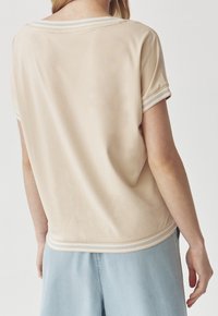 Beige kortærmet top med rund halsudskæring og lyseblå stribede detaljer ved ærmerne og kanten. Glat stof, afslappet pasform.