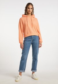 Felpa color pesco con un design testurizzato a coste, dotata di cordino e vestibilità oversize, abbinata a jeans azzurri chiari con risvolto e sneaker bianche.