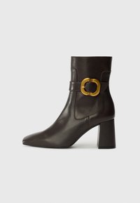 Brown leather ankle boot with a pointed toe, featuring a gold-tone buckle accent and a square heel design. Smooth texture, minimalist style.