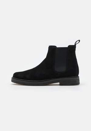 Black suede Chelsea boot with elastic side panels, pull tab, and textured sole. Classic design featuring a rounded toe and minimalist style.