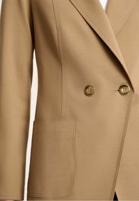 Beiger Doppelreiher-Blazer mit zwei runden Knöpfen, einem Reverskragen und einer einzelnen Tasche auf der Vorderseite, mit glatter Stofftextur.