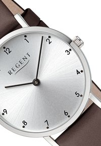 Montre ronde en argent avec finition brossée, chiffres noirs et bracelet en cuir brun fin. Couronne en argent et aiguilles simples pour l'affichage de l'heure.